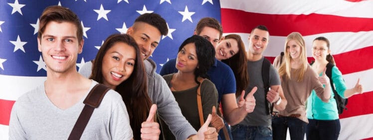 Advantages of Being a Student in America: 9 happy and diverse students stand in front of US flag with their thumbs up