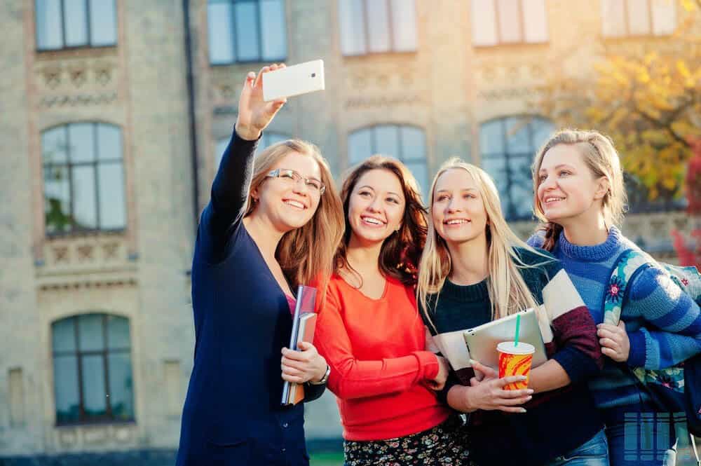 4 girl students holding books taking a group selfie
