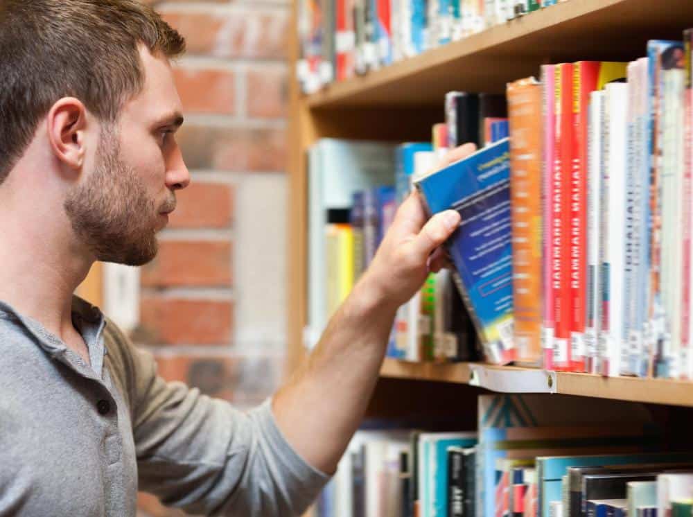 Student taking out a college textbook from a shelf